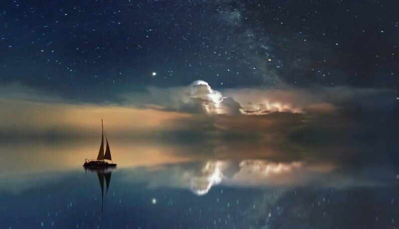 Serene night sky with stars reflecting on calm water as a lone sailboat floats peacefully under illuminated clouds.”