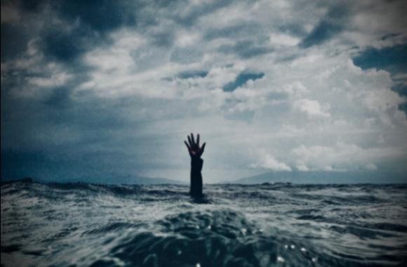 A hand reaching out of rough ocean water under a dark, cloudy sky
