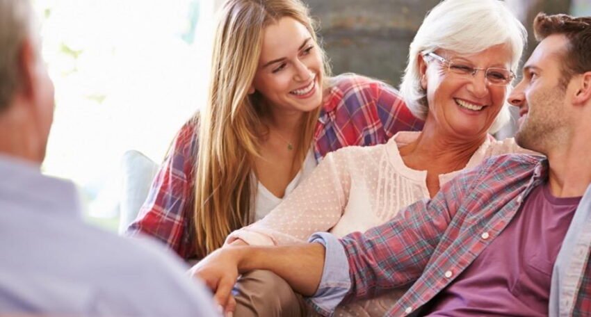 Smiling older woman sitting on a couch with her adult children, sharing a warm moment during a family counseling or consultation session.