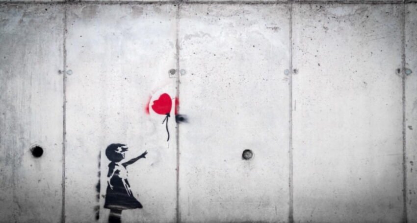 Black-and-white street art of a young girl reaching toward a red heart-shaped balloon on a concrete wall.